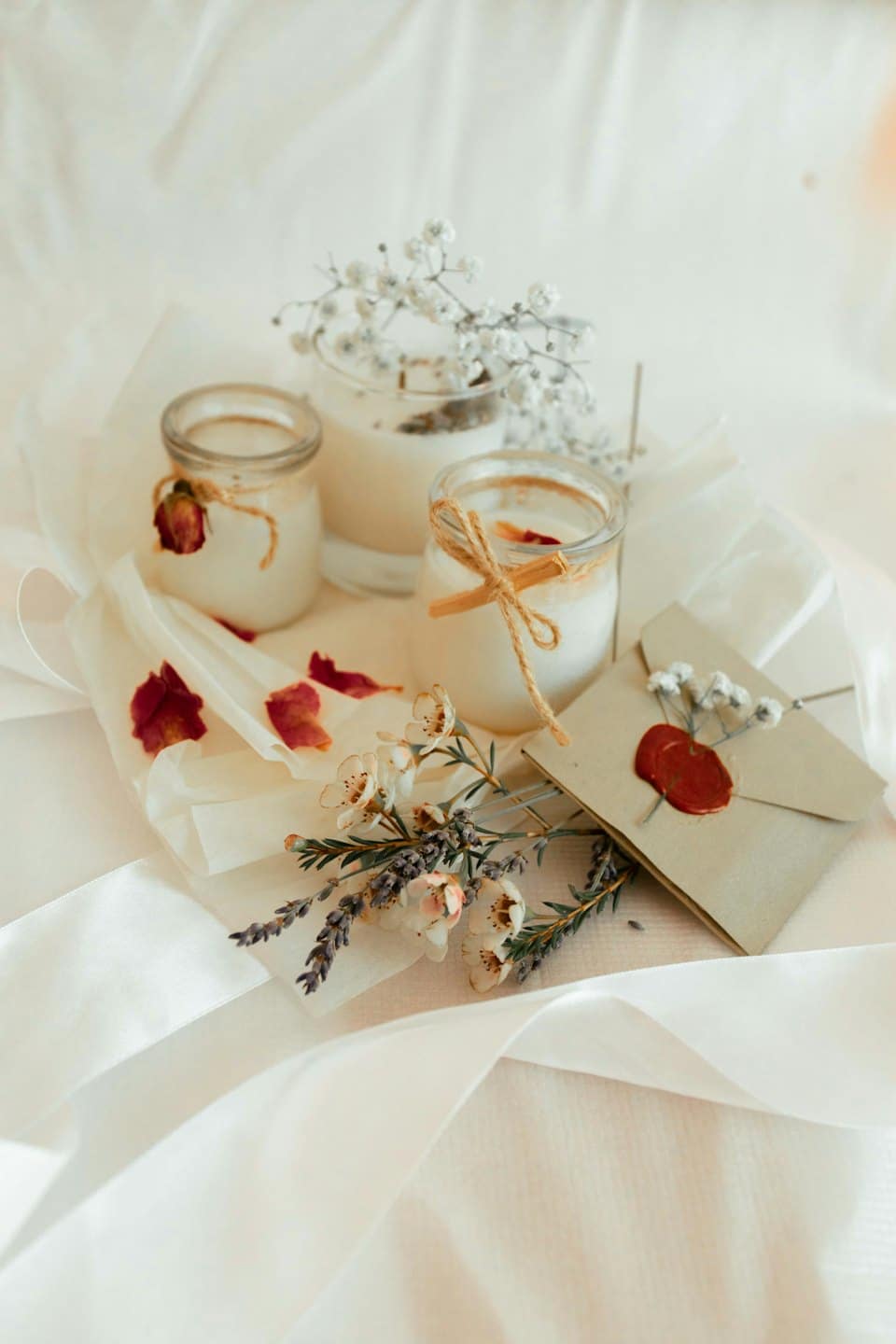 Tre candele artigianali in vasetti di vetro decorate con fiori secchi.