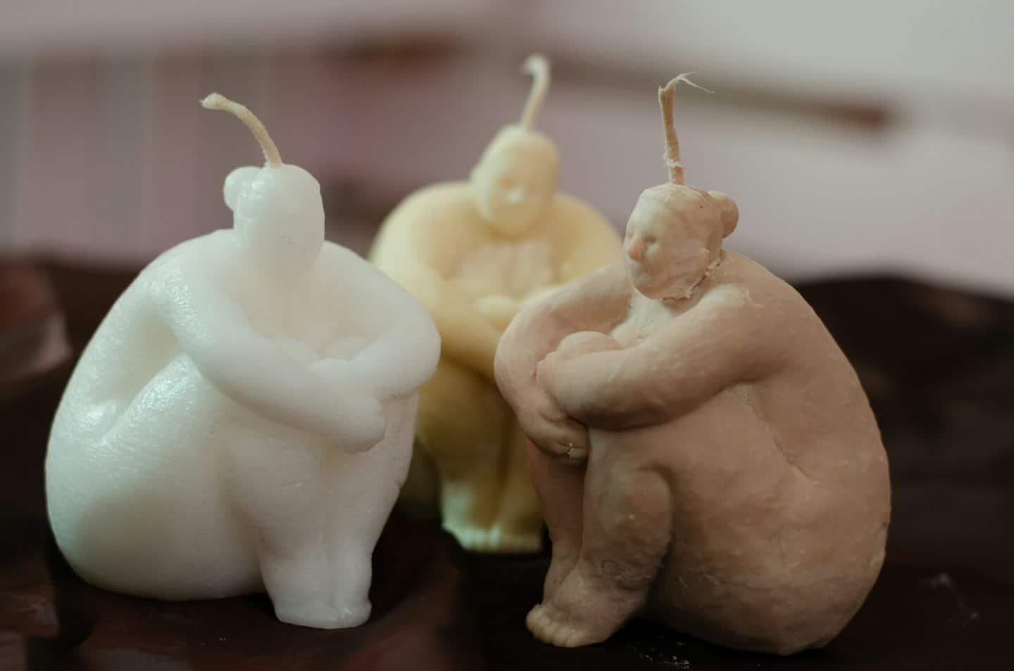 Tre candele di cera a forma di figura sono su una superficie scura.