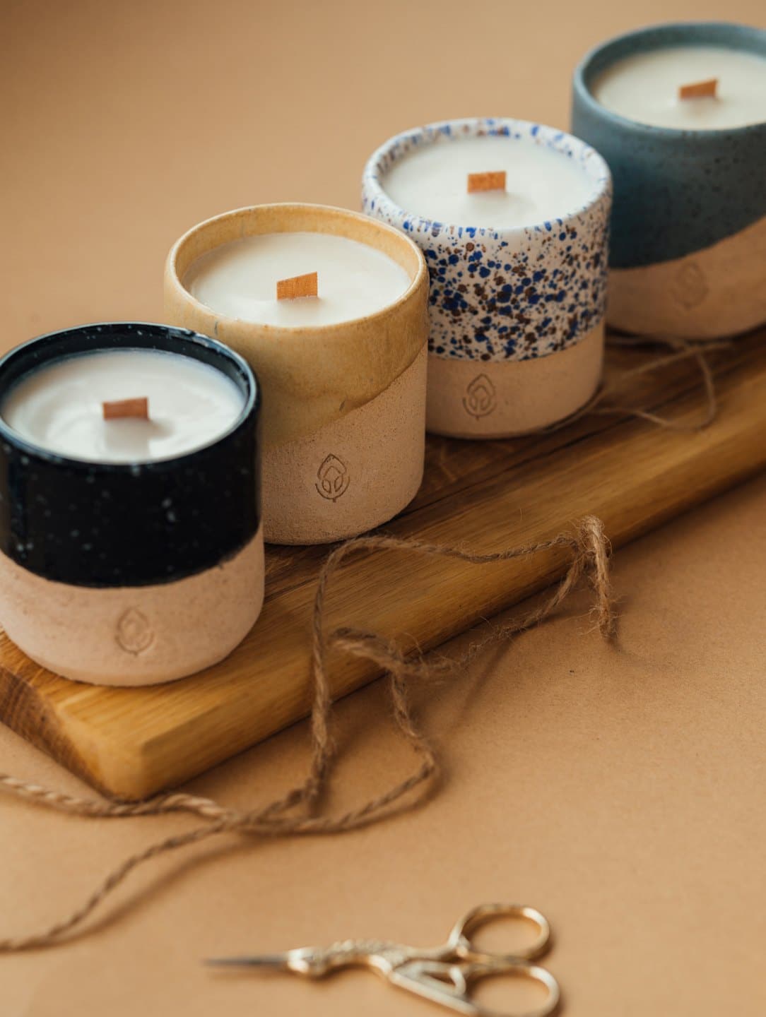 Quattro candele artigianali in ceramica disposte su un tagliere di legno.