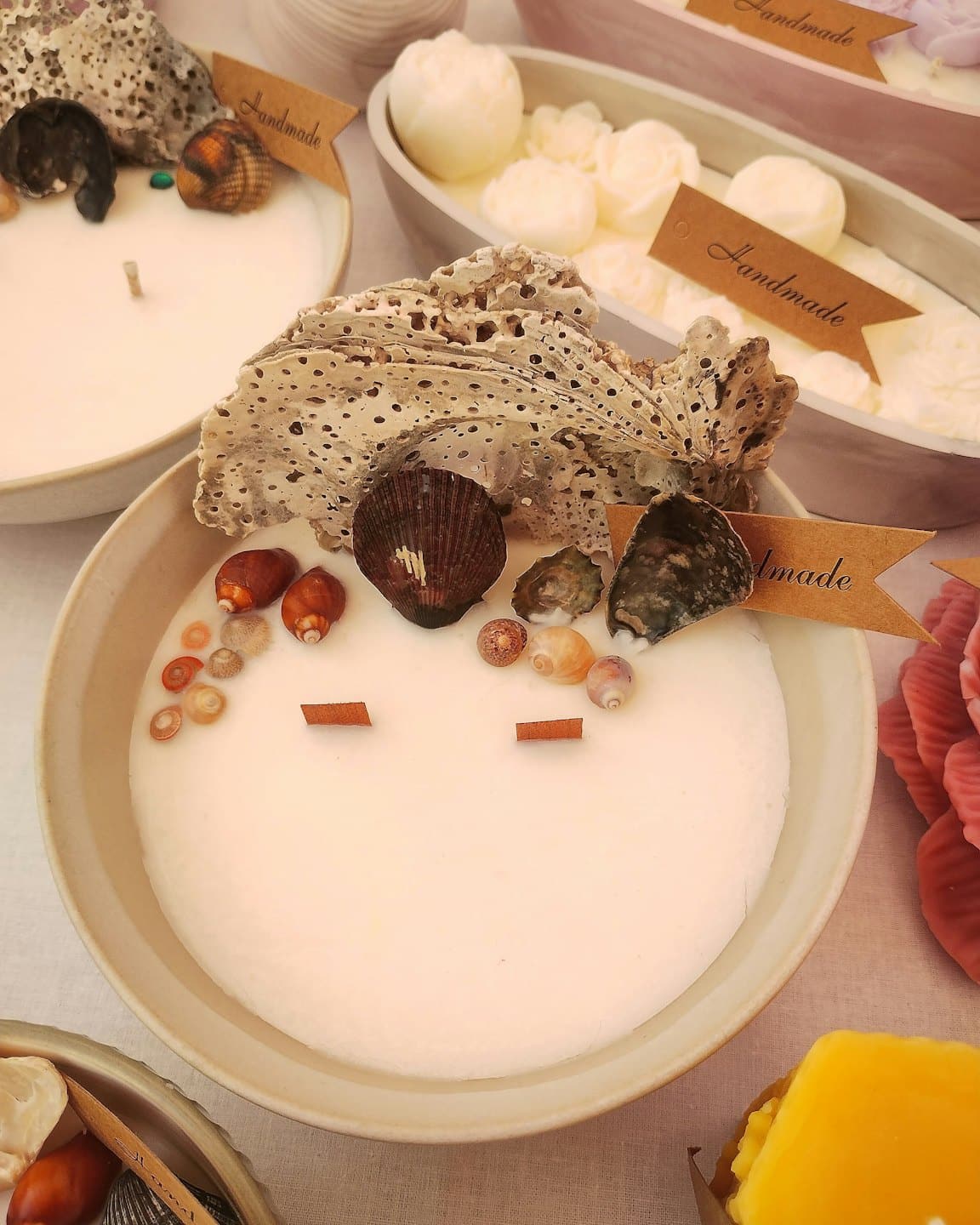 Candele artigianali in ciotole di ceramica decorate con conchiglie e coralli.